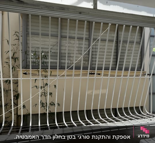סורגי מתכת לבנים על חלון עם צמחי במבוק ברקע
